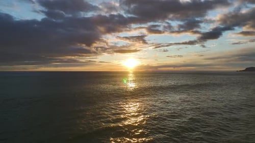 Aerial Video of Fiery Golden Sun Setting Over Ocean Horizon With Purple Clouds Above