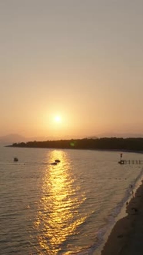 Golden sunset over the calm sea with boats and a distant coastline