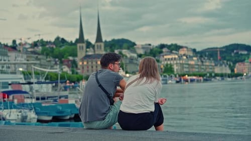 Couple Sitting on the Shore of Lake Lucerne with the City of Lucerne in the Background in Summer