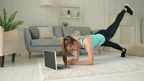 Eine junge Frau, die während der Quarantäne zu Hause online über den Laptop trainiert
