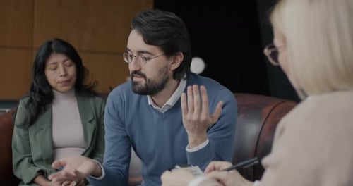 Unhappy Husband Talking to Psychologist During Couple Therapy Session While Wife Listening in Office