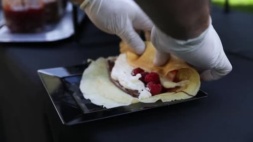 Crepe being folded with cream, raspberries, and sauce, close up
