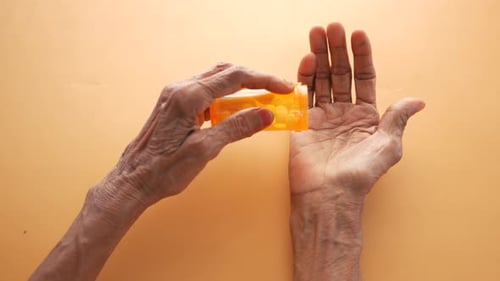 Top View of Senior Women Taking Pills From a Orange Color Container