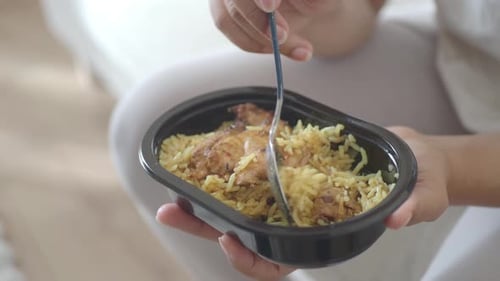 Comer pollo y arroz de un recipiente negro en casa