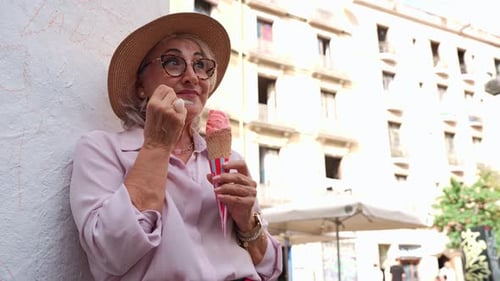 Senior Woman Enjoying a Pink Ice Cream Cone in an Urban Setting