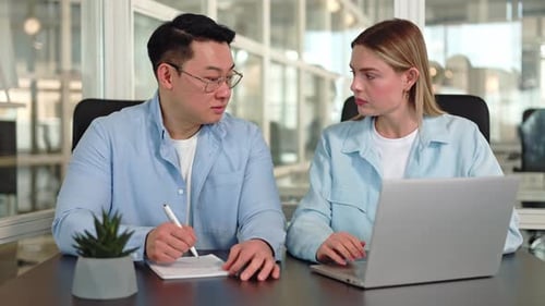 Two Coworkers Using Laptop and Making Notes in Notebook in Office Interior