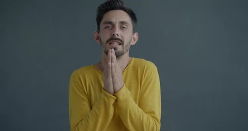 Zeitlupenporträt eines emotionalen jungen Mannes, der bettelt, bettelt, Hände zusammenlegt und nach oben schaut