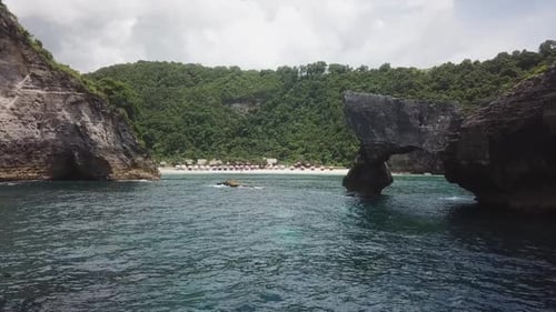 low water level aerial past rugged stone cliffs to tropical beach