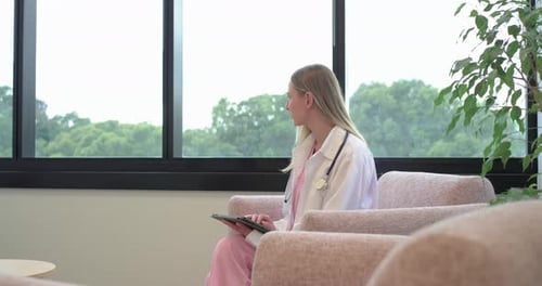 Ärztin im Peeling und Stethoskop klopft in der Klinik auf Tablette, schaut aus dem Fenster, Beratungsnotizen