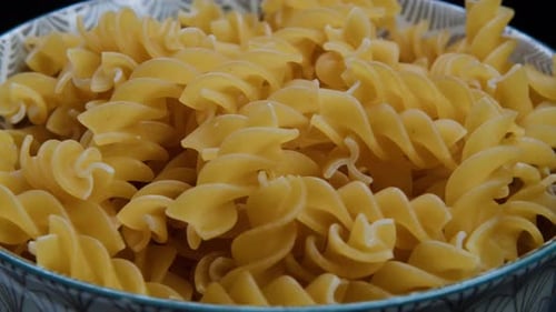Bowl of uncooked golden fusilli pasta, close up