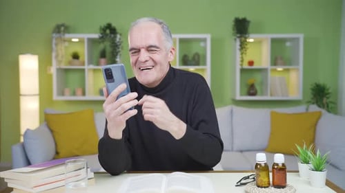 Senior Smiling Using Smartphone at Table Indoors
