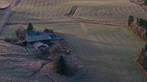 A Farmhouse and Barn Sit Beside Neatly Lined Fields Stretching Across a Quiet Rural Landscape -