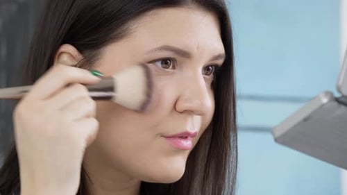 Pretty women applying make-up with a brush and smile to the camera, close up