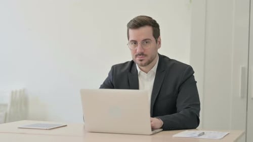 Geschäftsmann lächelt in die Kamera, während er Laptop benutzt