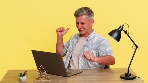 Adult Man Celebrating Gaming Victory at Laptop with Raised Hands Happy Face While Sitting at Table