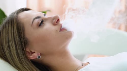 Femme exhalant de la fumée provenant d'une cigarette électronique