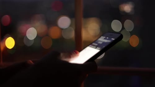 Person Using Phone with City Lights at Night