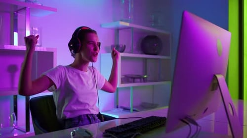 Happy gamer girl celebrating victory in cyberspace studio neon lights at home