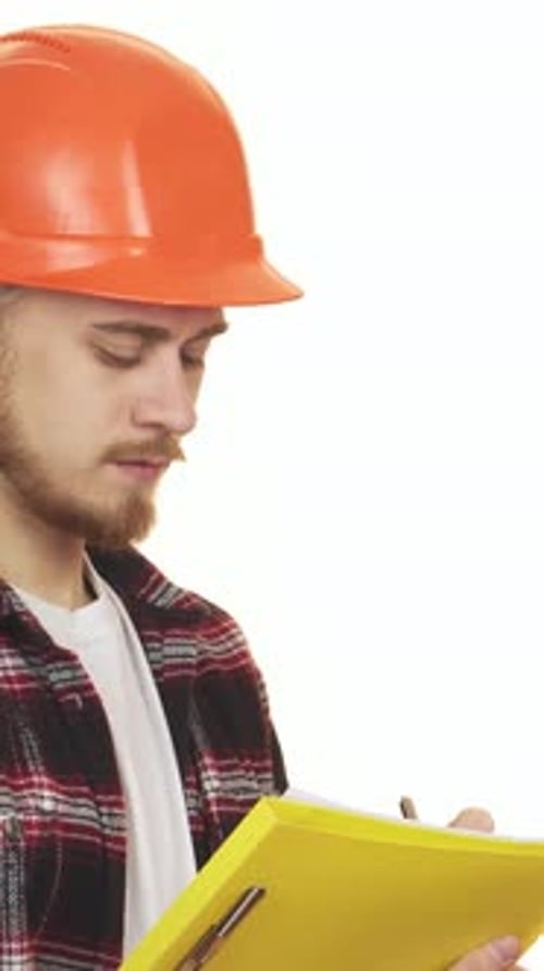 Cheerful Young Male Contractor in Hardhat Taking Notes with Clipboard