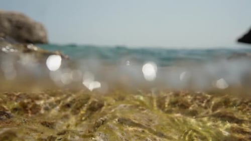 The camera lies on a rock at the edge of the sea, and a wave washes over it, in slow motion.