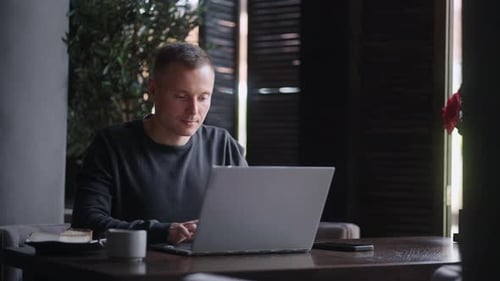 Travailleur indépendant masculin travaillant avec un ordinateur portable dans un café, portrait moyen, travail et divertissement sur Internet