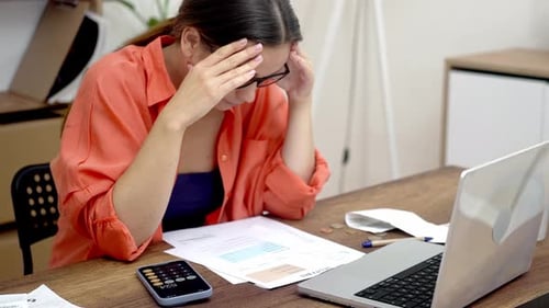 Stressed Woman at a Table Looks at Paper Bills Perplexed By the High Payment Rates