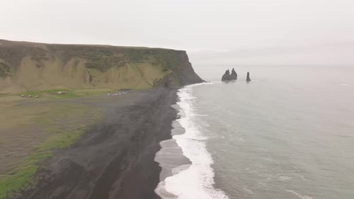 Aerial shot of the black sand beach at Reynisfjara, Iceland, with waves crashing against the shore a