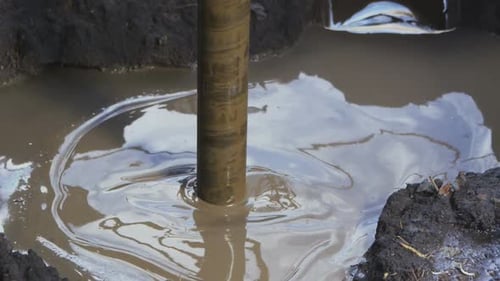 Metal Drill Makes Hole in Ground with Water Puddle