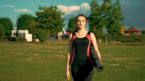 Athletic Woman Walking with Yoga Mat in Park