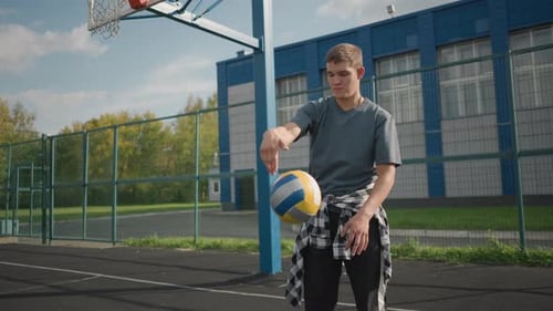 Sporty Man Slams Volleyball on Outdoor Court with Building and Greenery Background