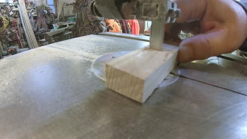 Using a bandsaw to cut small blocks of wood; view along the table of the bandsaw and end of the stri