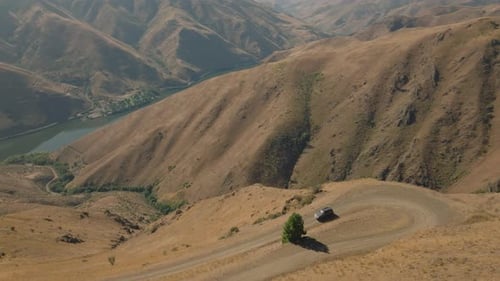 Aerial tracking car on steep road going down hill in massive river canyon