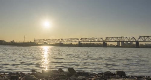 Timelapse of City River Bank Sun Rays Blue Sky and Railway Bridge Over Horizont Summer Sunset Time