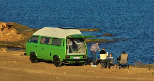 Group of People Relaxing in Nature with a Motorhome Standing on a Cliff Above the Sea Holiday in a