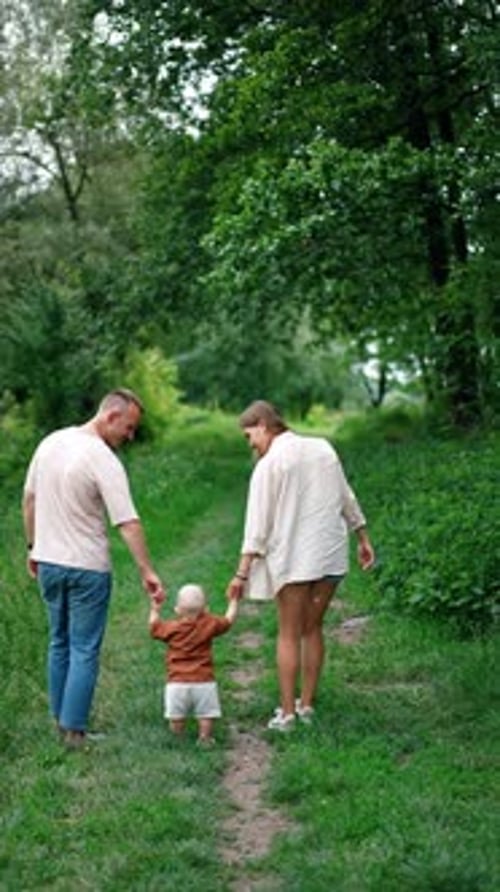 Mother and father leading their baby boy learning to walk. Family of three in the nature in summer.