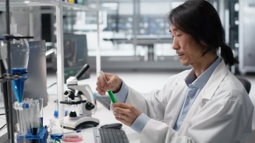 Senior Biochemist Shaking Laboratory Glassware Filled with Green Solution