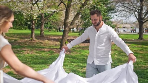 Married couple are stretching out a blanket preparing to have a family picnic in a park