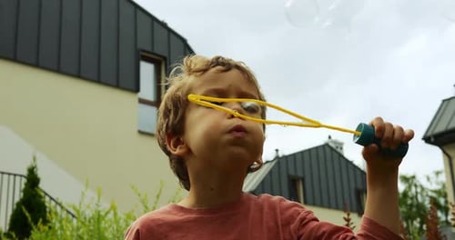 Kleiner Junge mit lockigem Haar bläst Seifenblasen durch eine Plastikschlaufe mit ernstem