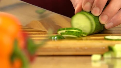 Man's hand cutting cucumber. Male hands slice green cucumber using sharp knife.