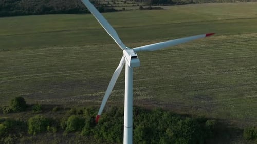 Aerial drone shot around single wind turbine generator in grass field