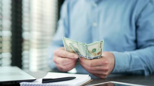 Close up. Male hands count one hundred dollar US bills. Mature businessman in blue shirt counting