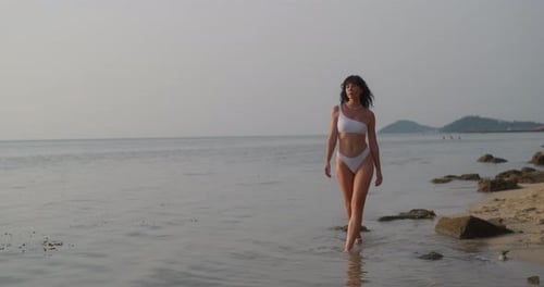 Portrait of Woman in White Bikini Walks Along Sea Shore on Twilight Beach