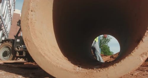 A construction worker passes across a job site and is visible through a concrete tube.