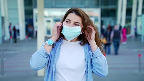Portrait young attractive curly hispanic woman put on a protective medical mask on urban city