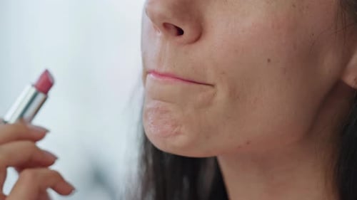 Woman applying pink lipstick in close up