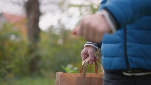 Primer plano de una persona que camina al aire libre sosteniendo una bolsa de papel con vegetación vibrante