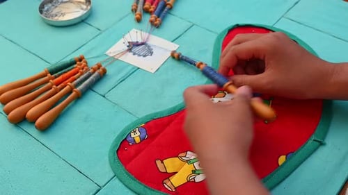 Hands of child making bobbin lace. Colorful lace threads. Real time.