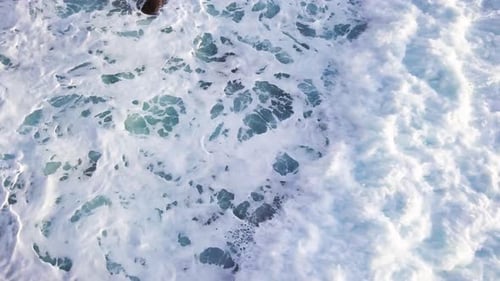 Top down aerial view of waves crashing and creating abstract foam patterns on sea. Static shot.