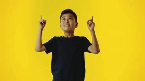 Boy Points Upward on a Yellow Background