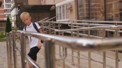 A Cheerful Little Schoolboy with a Backpack Slowly Walks Up the Stairs to School